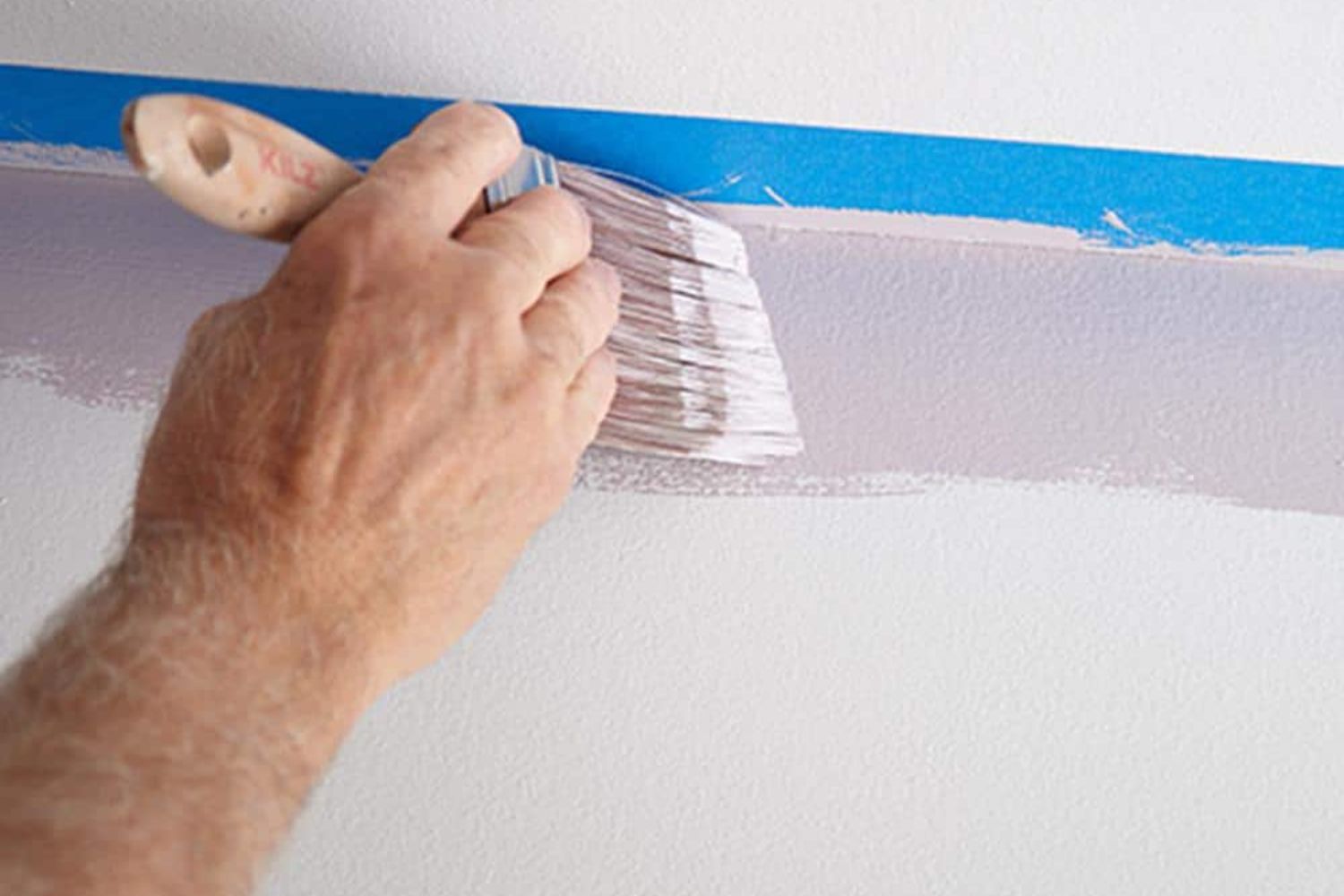 A person running a paint brush along a piece of painter's tape to add color to a wall using the best-VOC paint.