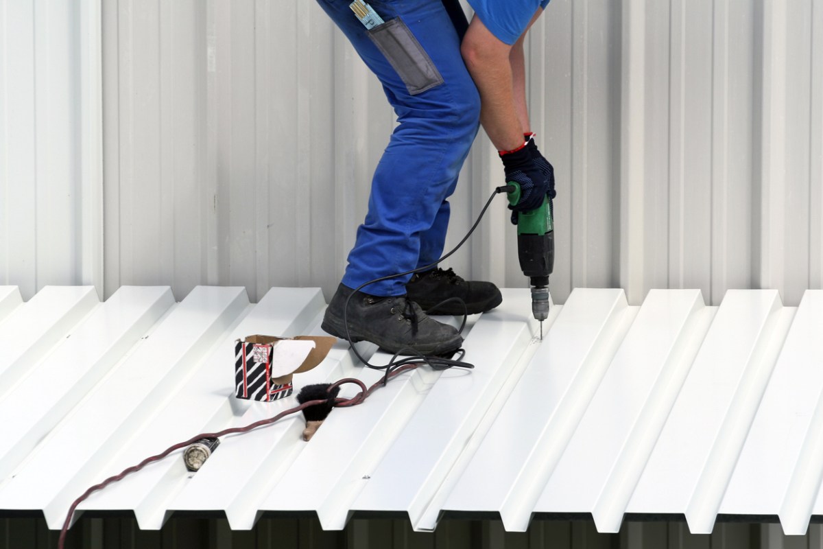 A close up of a worker in a blue worksuit using a tool to install a roof.