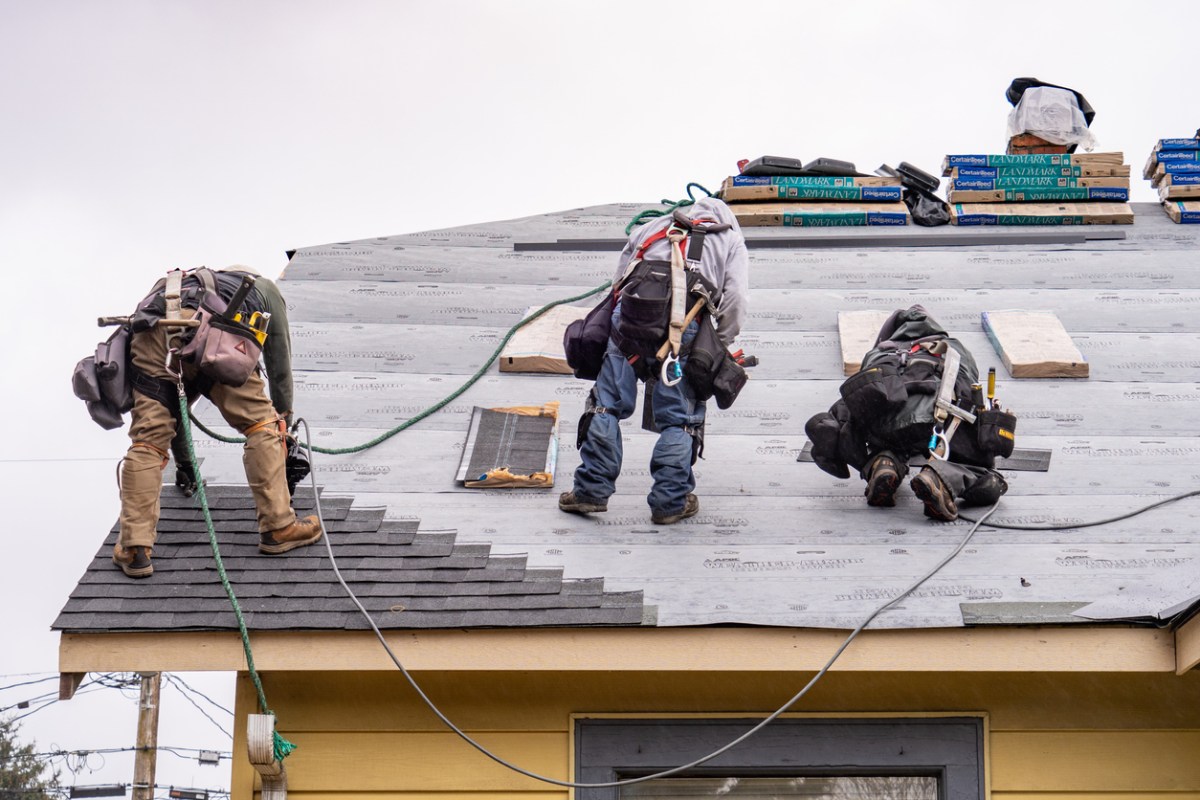Three roofers work on a installing a roof.