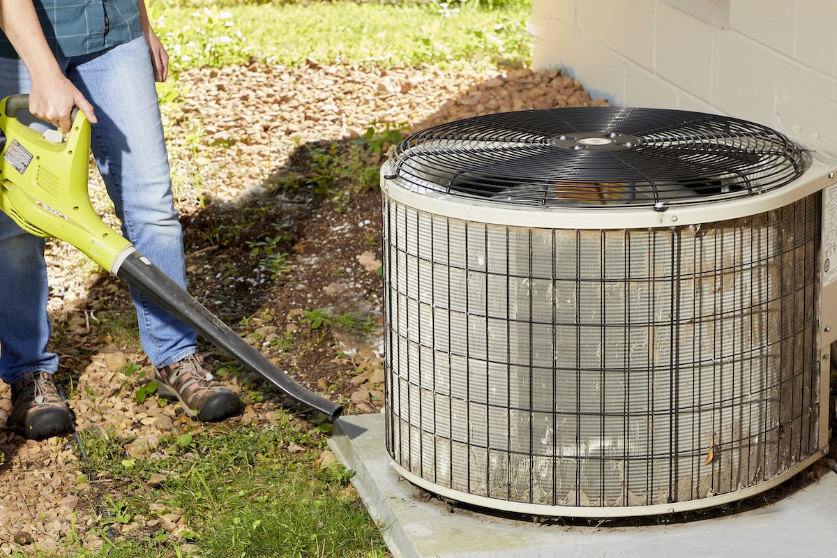 A homeowner cleaning around an air conditioner condenser unit to troubleshoot an air conditioner that stops cooling.