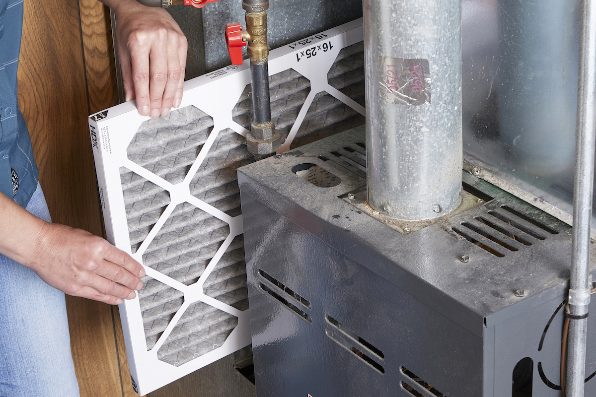 Woman removes dirty air conditioning filter from unit.