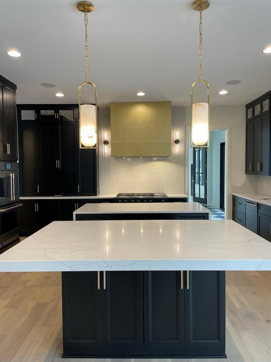 A sleek brass, rectangular range hood lies at the far end of a sleek modern kitchen with navy cabinets and marble counters.
