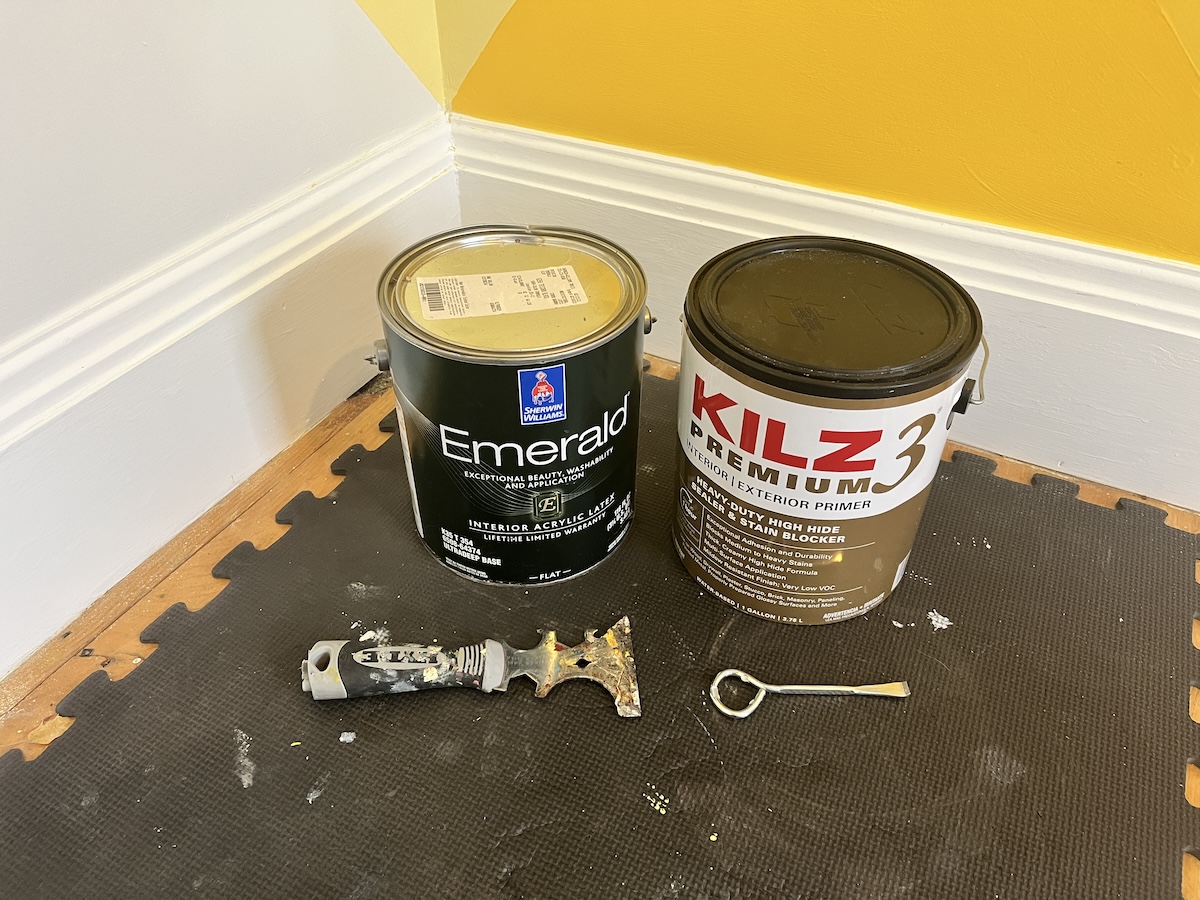 Cans of paint near yellow wall and can openers.