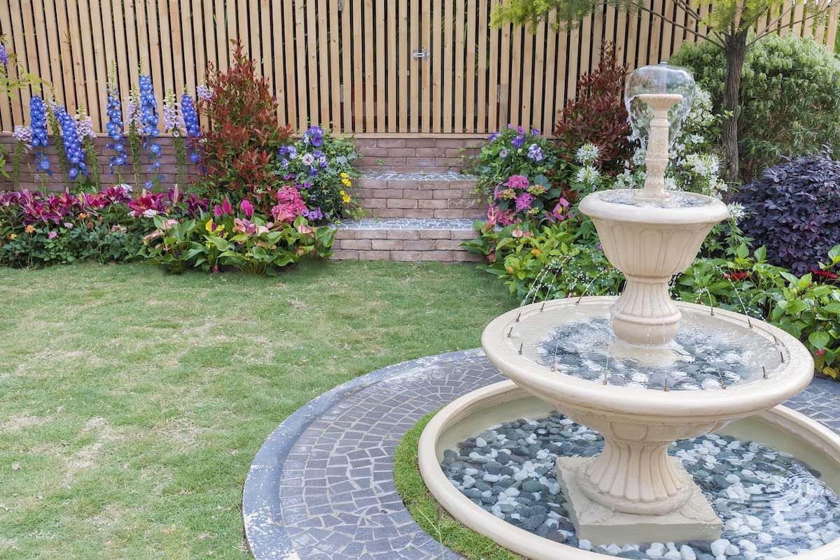 A fenced-in backyard with colorful flowers and a multi-tiered fountain.