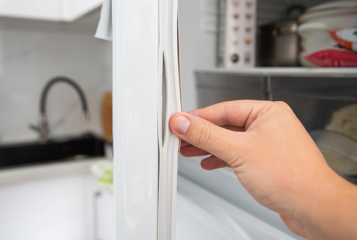 Person pulling on a torn gasket on a freezer.