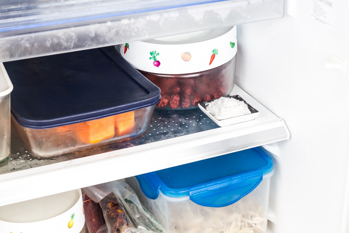 Inside of refrigerator with shelves full of food in glass and plastic containers, with powdered deodorizer in small dish. 