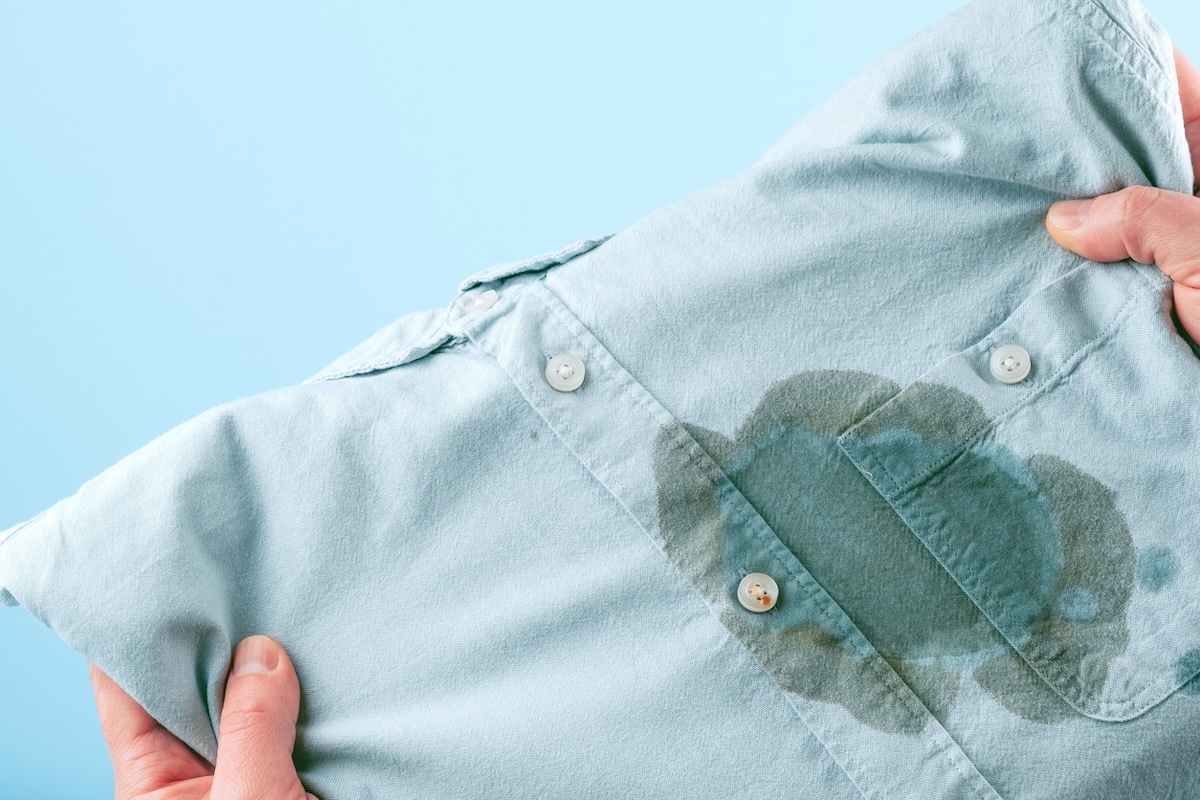 Person holding a blue button-down shirt with a grease stain on the chest.