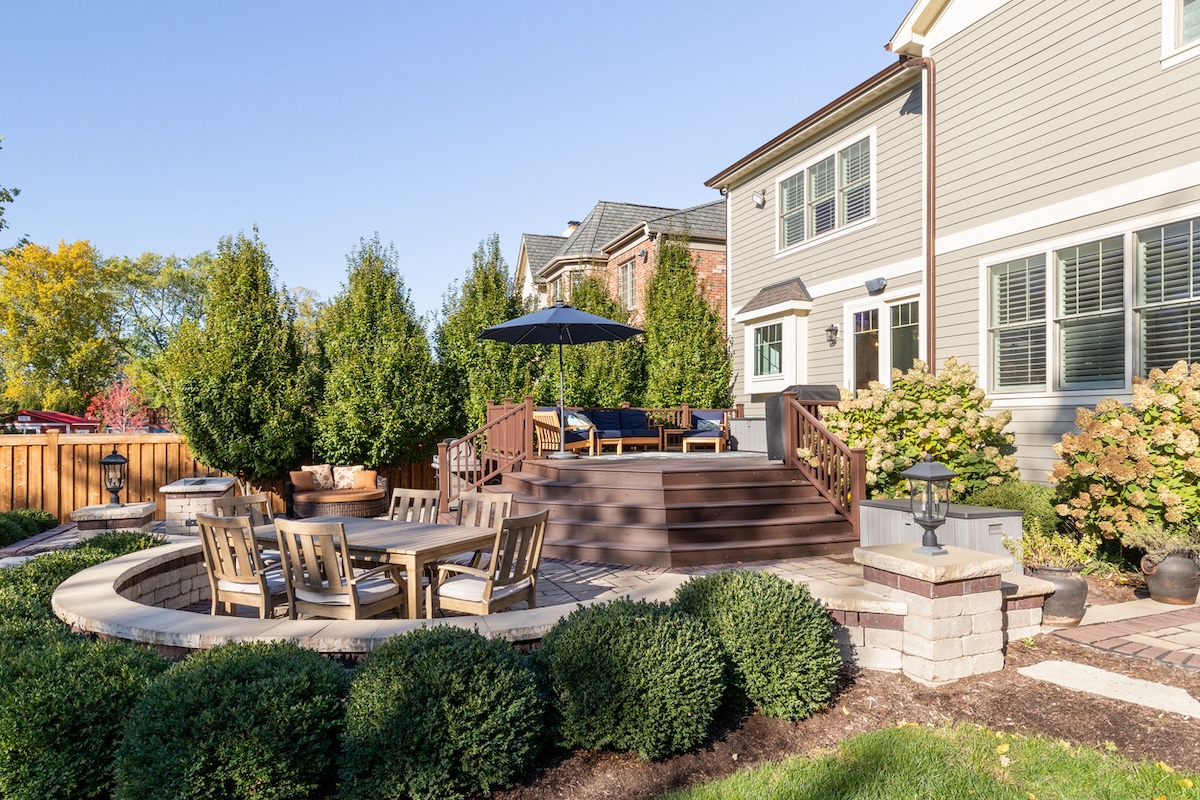 The backyard of a home with a large deck, stone patio, and outdoor furniture.