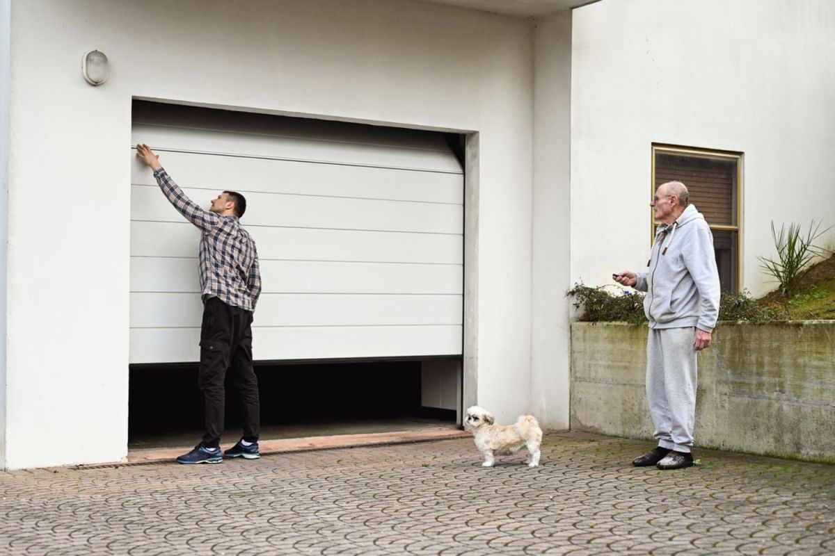 Two men and a dog stand in front of a garage door.