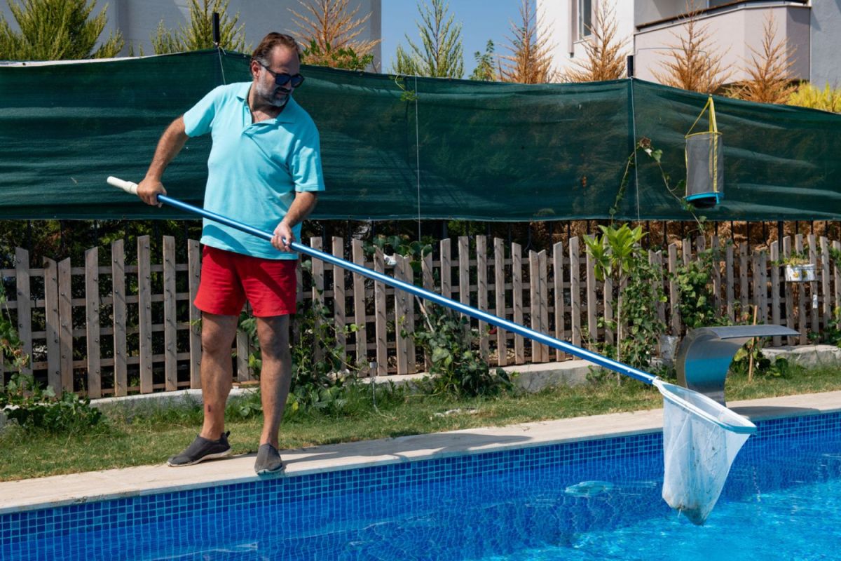 A man uses a net to clean a pool.