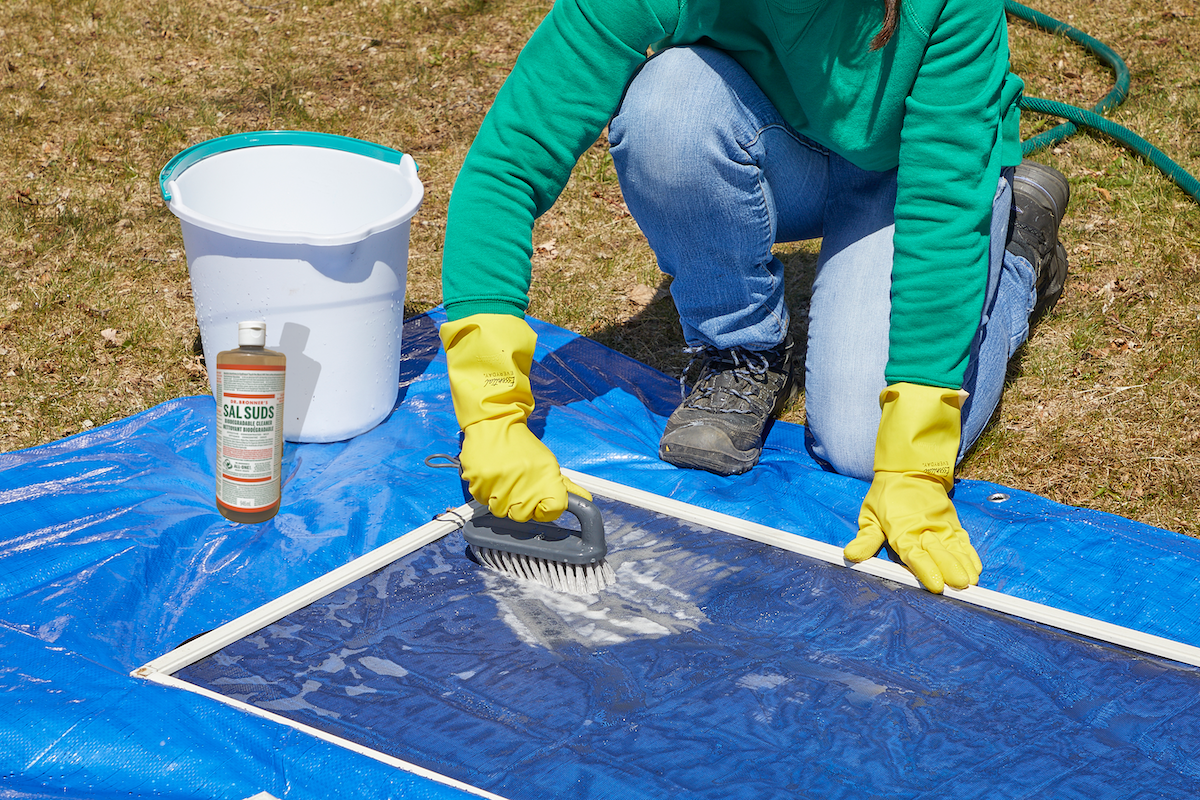 A person using Dr. Bronner's Sal Suds to scrub window screens.