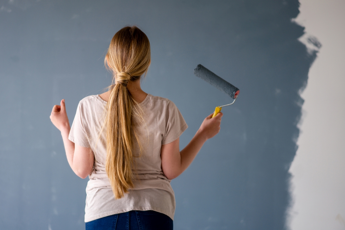 Woman looking at dark painted wall with paint roller in hand.