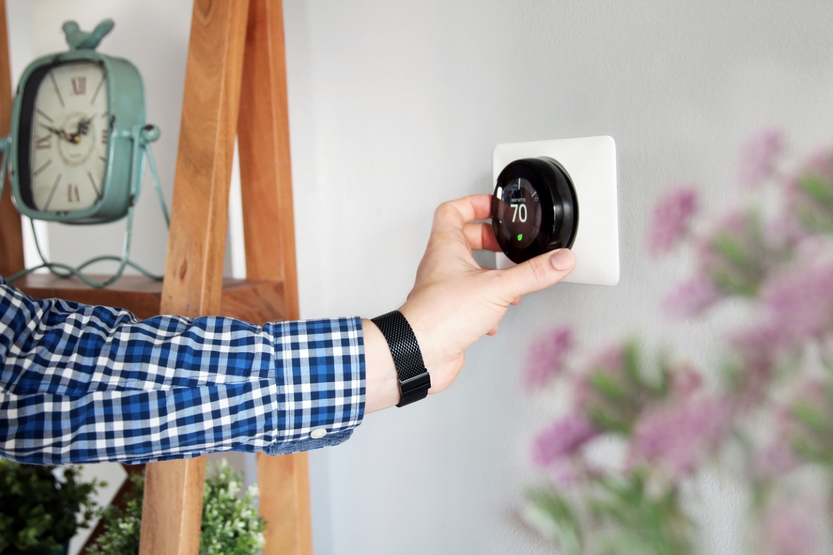 Man adjusting temperature on a smart thermostat on wall.