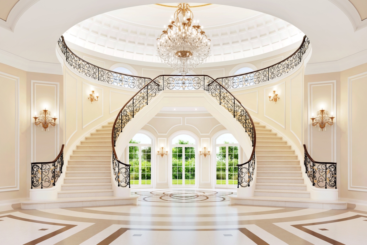 A white double staircase dominating the grand foyer of a bright mansion.