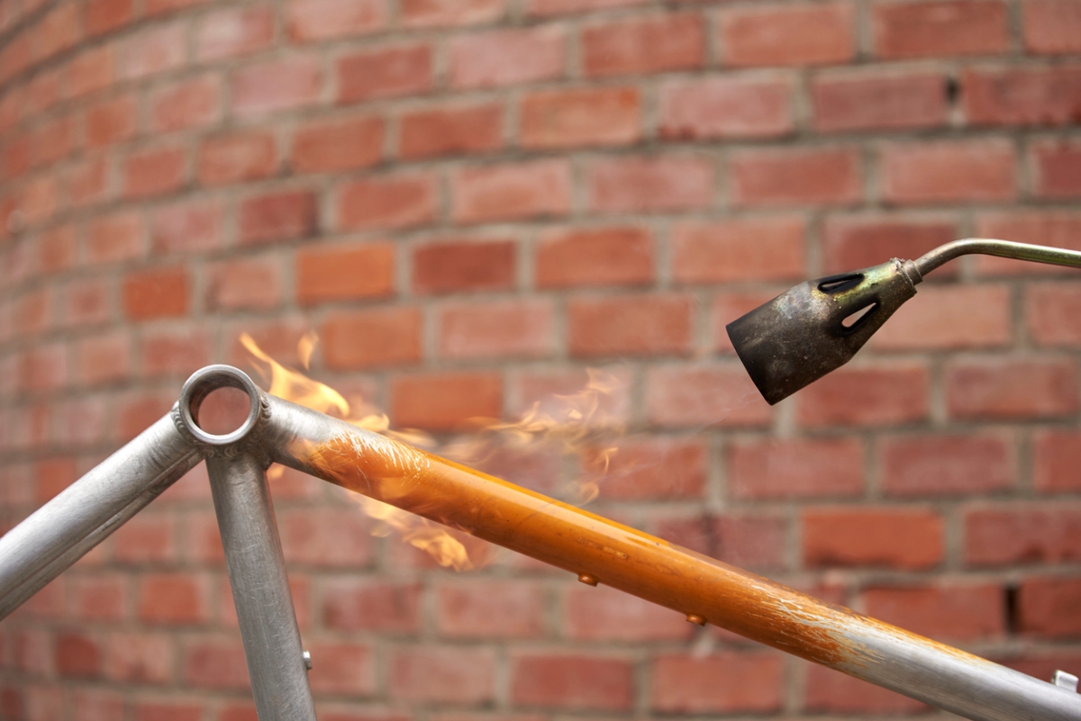 Using a torch to remove orange paint off metal bike.