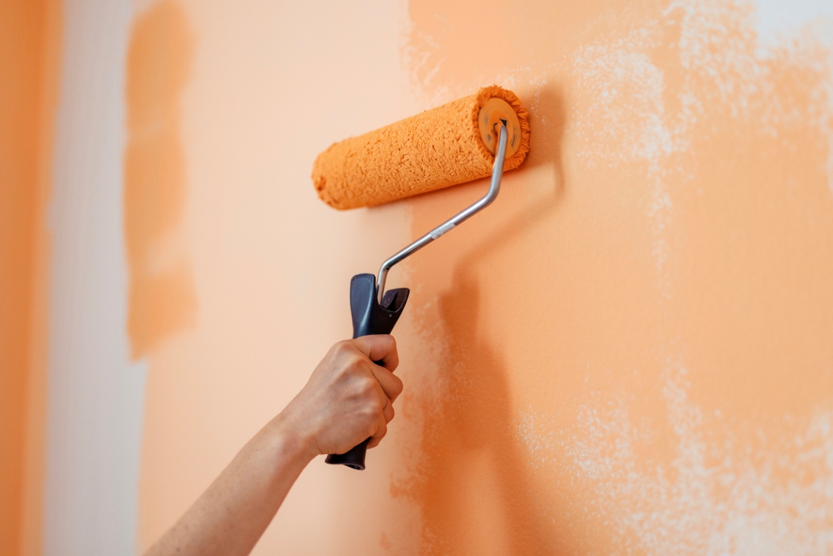 Hand of person with paint roller on wall.