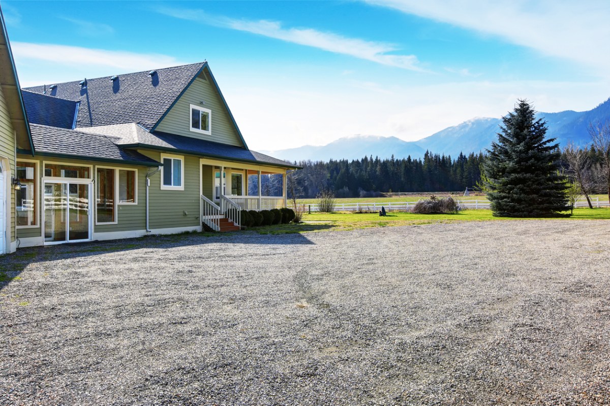 A-home-in-the-mountains-has-a-large-gravel-driveway-in-front.
