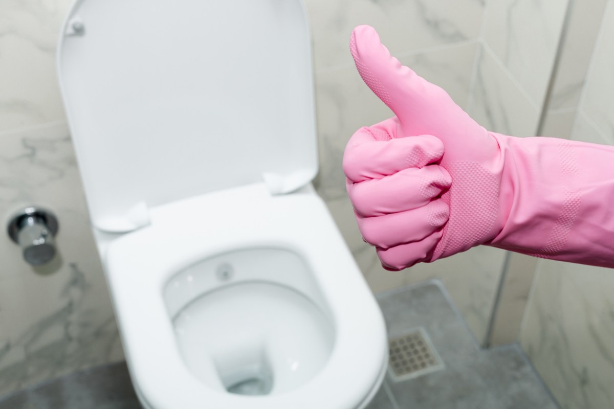 A pink-gloved hand giving the thumbs-up sign in front of a clean toilet with the lid up.