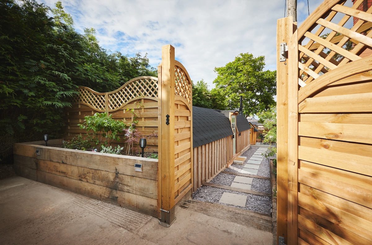 A light-colored lattice wood fence with a large open gate leading to a paved walkway.