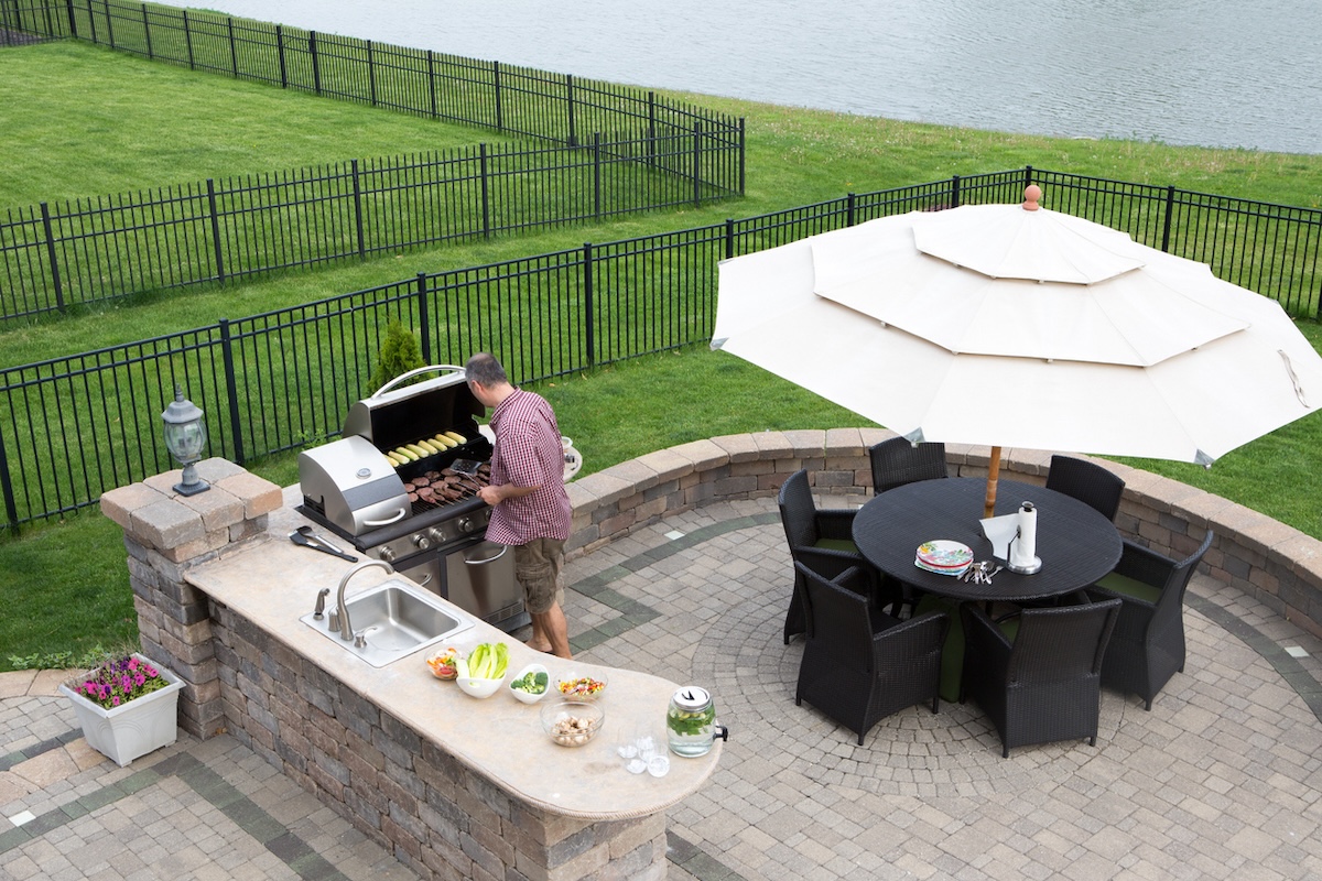 A mature man cooking on a grill in an open-air outdoor kitchen with a complete covered patio set.