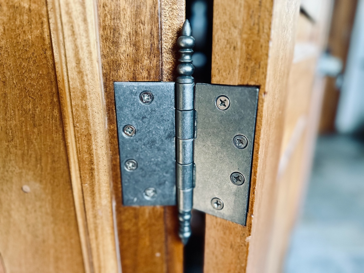 A metal antique-looking door hinge on a brown wood door.