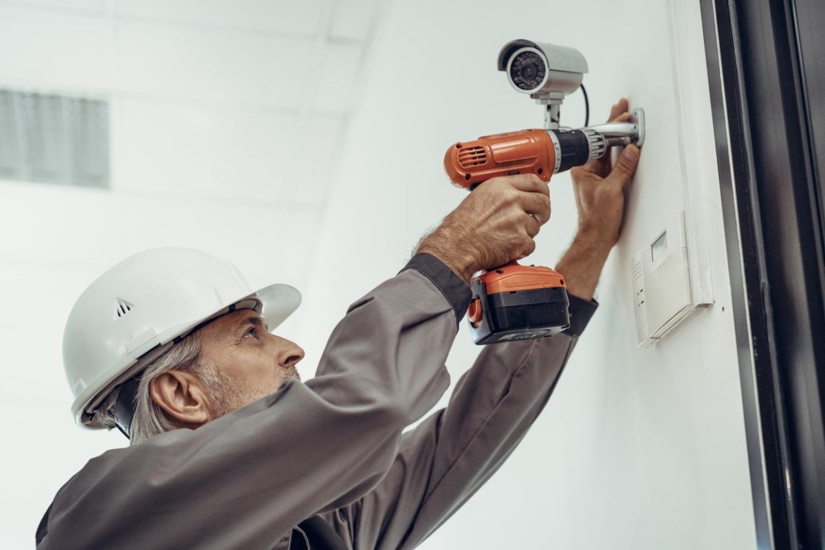 A worker in a white hard hat installs a security camera. 
