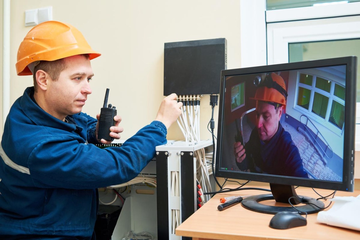 A worker in an orange hard hat assesses a security system video feed. 