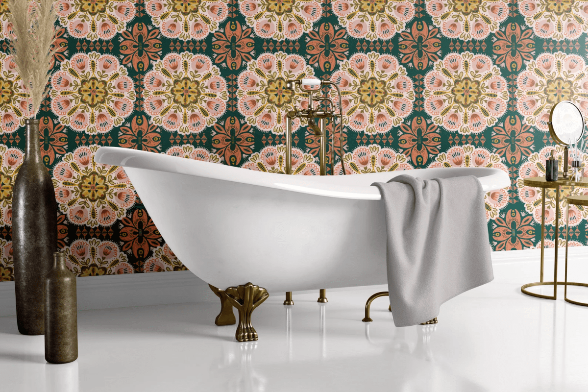 A claw foot bathtub sits in front of wallpaper with a green and orange medallion pattern.