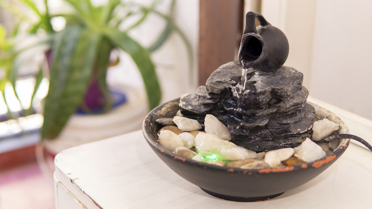 Dark stone tabletop Zen water fountain with stones inside, with a plant in the background.
