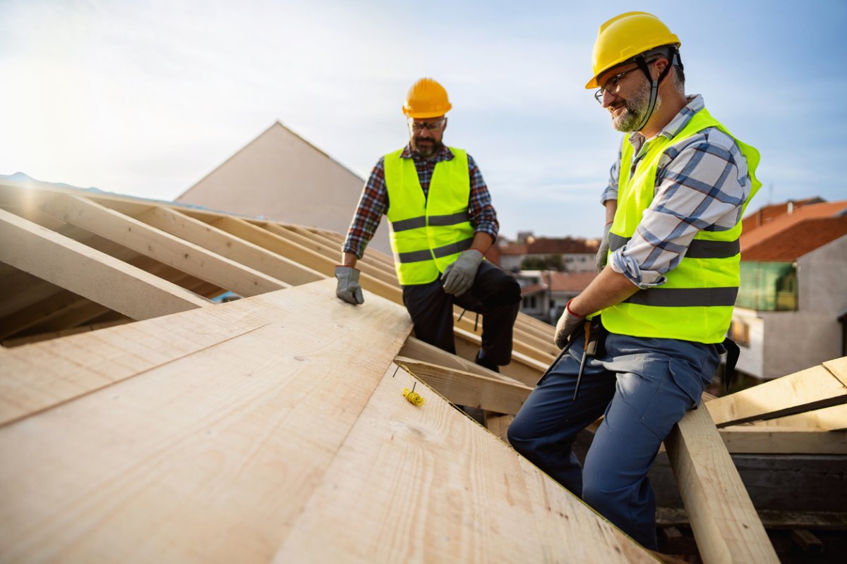 Two men in yellow hard hats construct a roof. 