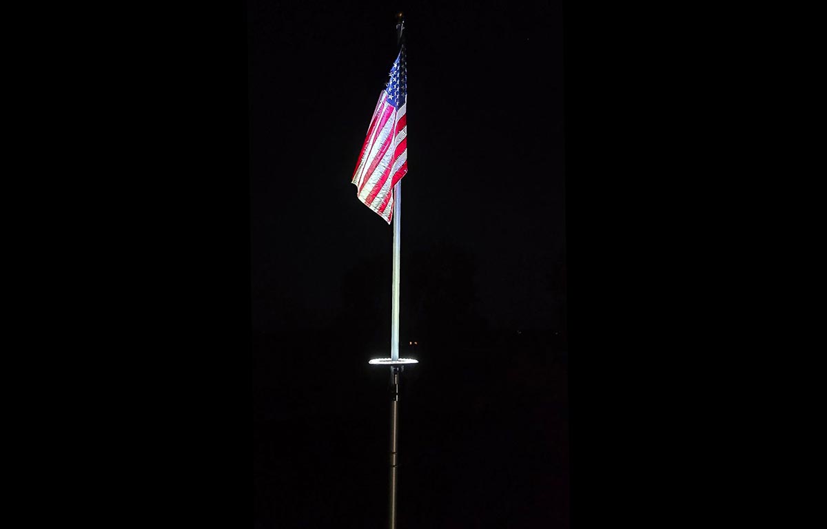 The Kayiune Solar Flagpole Light lighting the American flag on a dark background.
