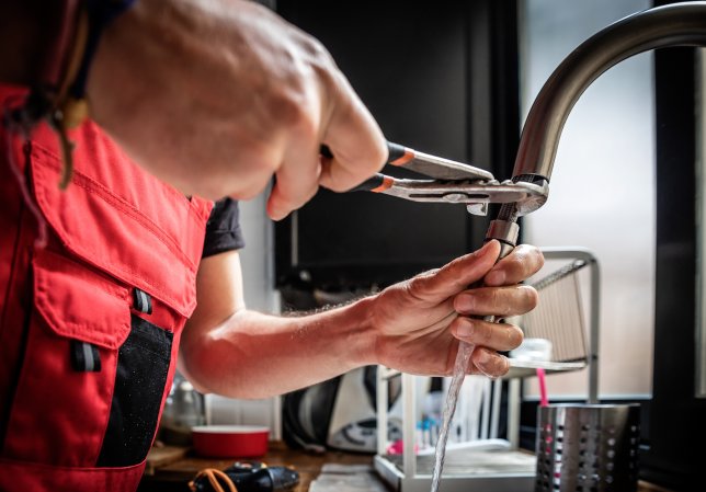 A-persons-hands-use-pliers-to-fix-a-kitchen-faucet.