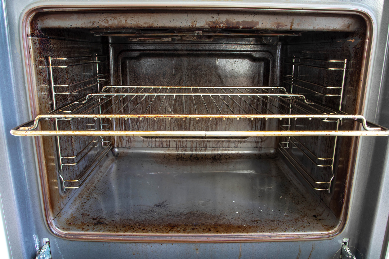 A dirty oven rack sits partially pulled out of a even dirtier oven.