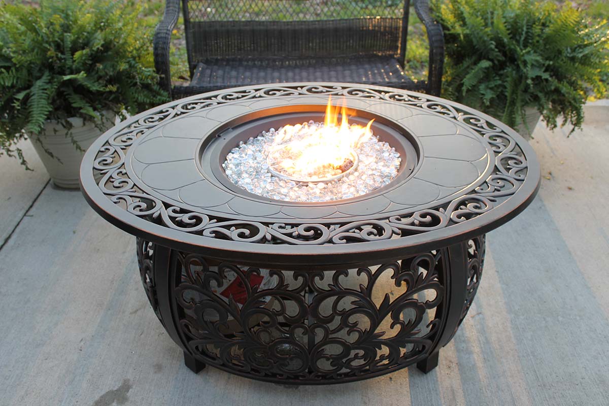 The Fleur De Lis Living Slattery Propane Fire Pit Table burning a fire on a patio.