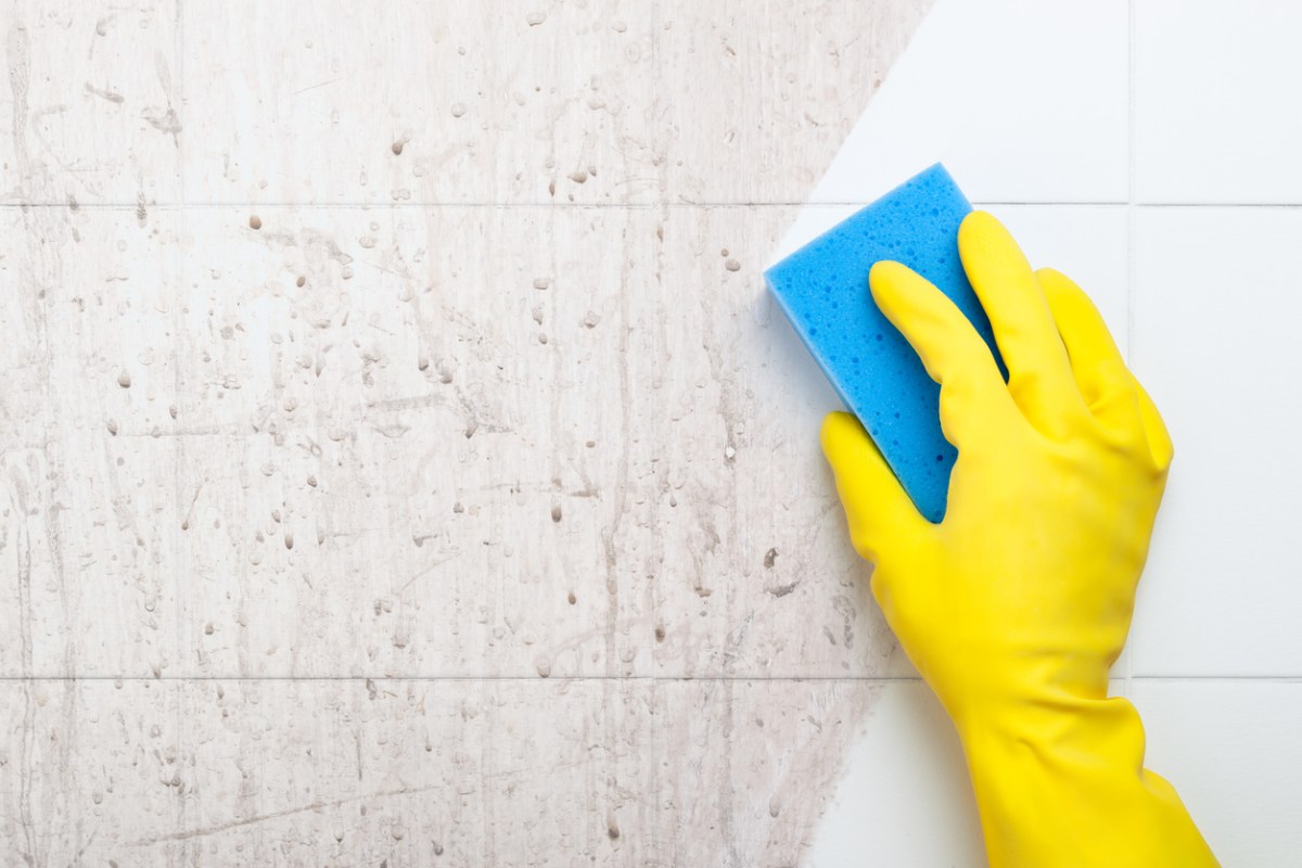 An unseen person wipes away shower wall tile grime, leaving behind a clean white streak.
