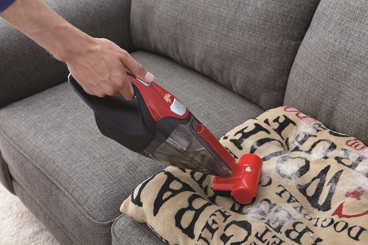 A person using the best handheld vacuum for pet hair to clean pet hair off a couch pillow.