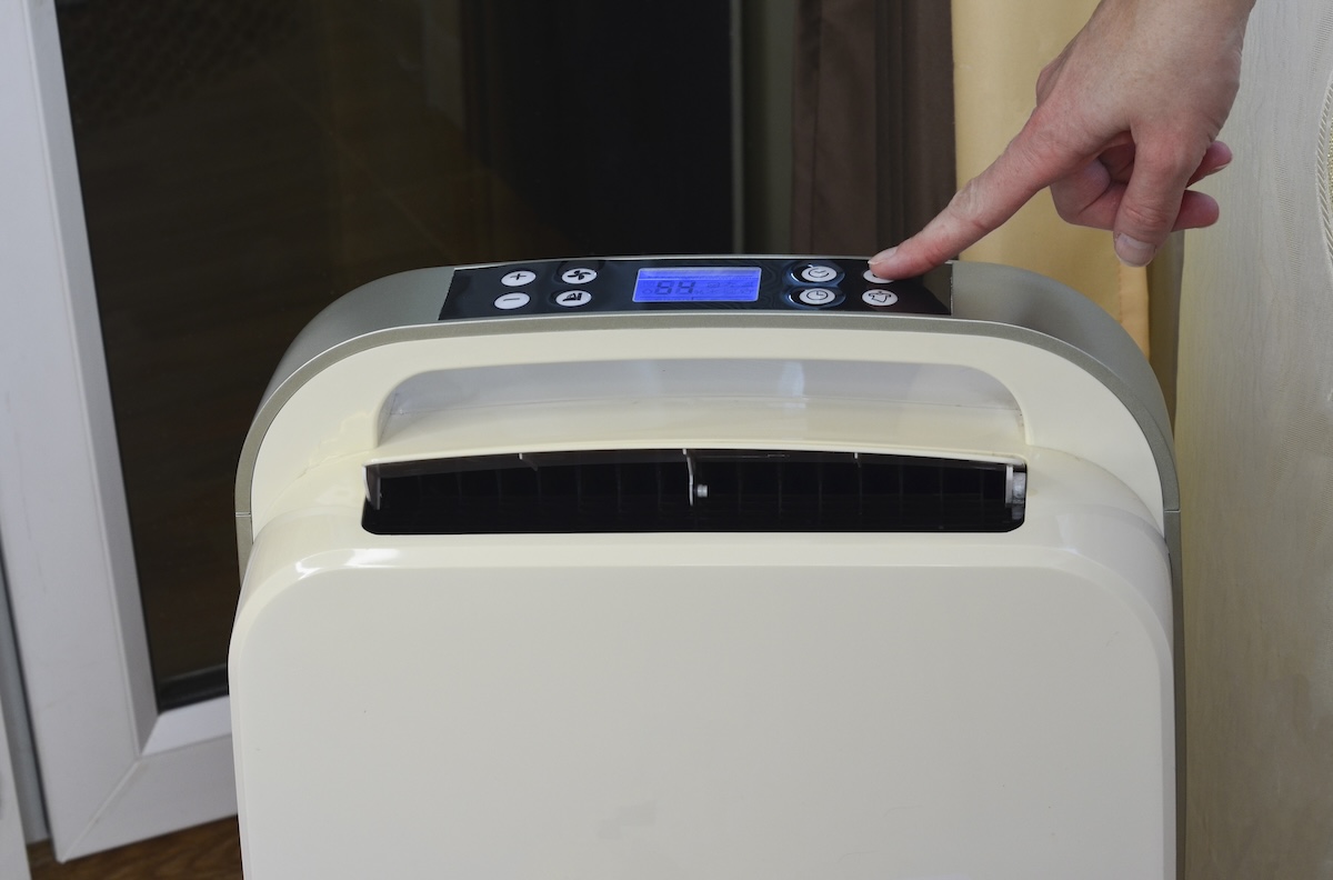 A person pushes the button on a dehumidifier. 