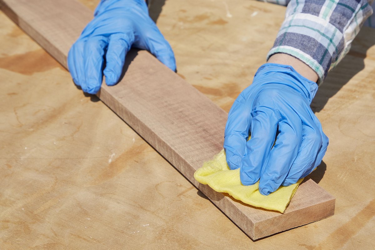 Woman removes dust from sanded piece of wood with a tack cloth.