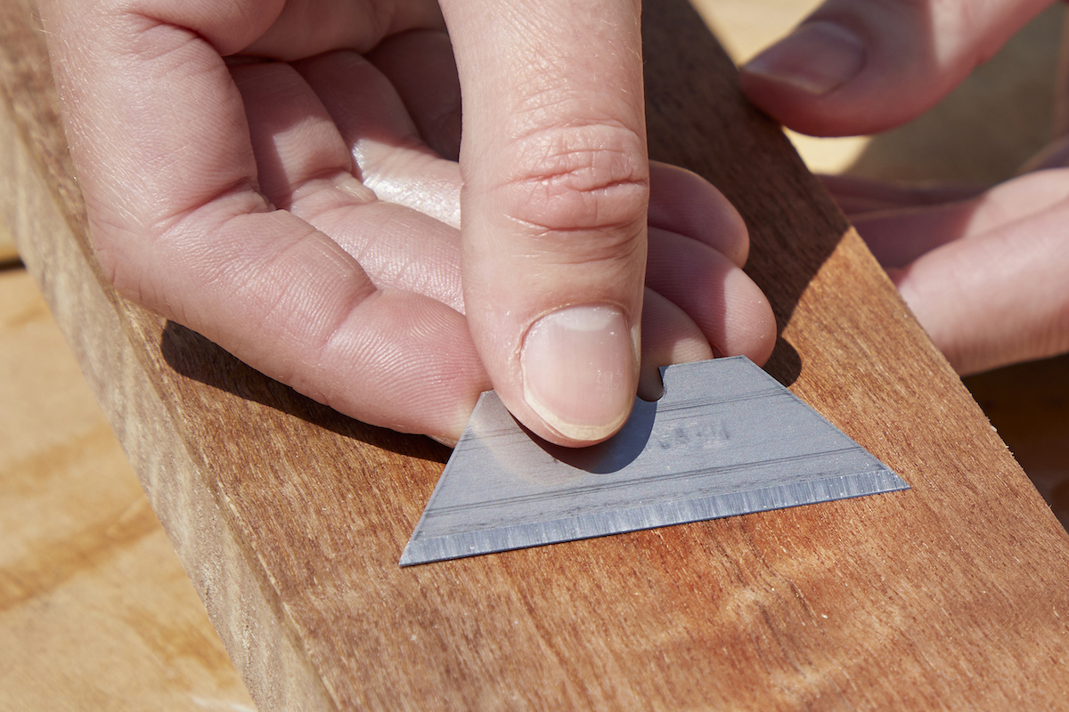 Woman uses a razor blade to remove imperfections in a fresh polyurethane coat on wood.