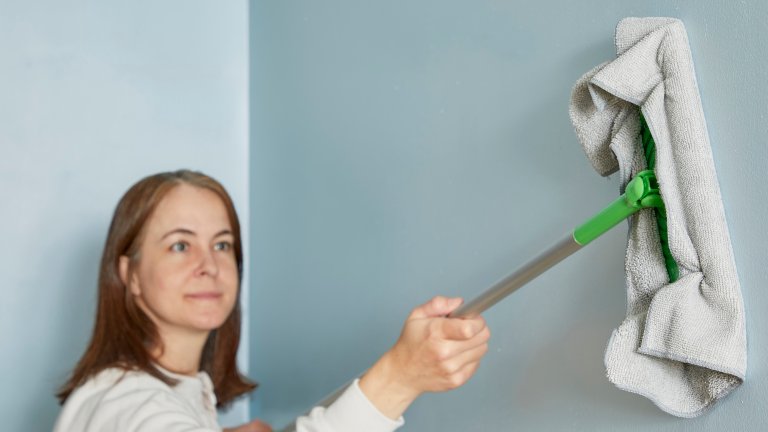 Woman uses a rag over a dry mop head to clean walls.