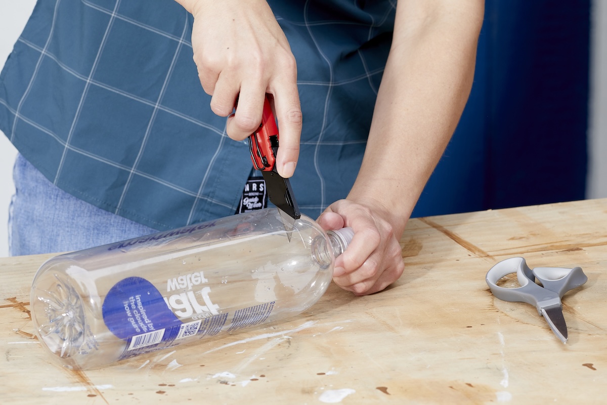 Woman cuts a plastic drink bottle at the top with a utility knife.