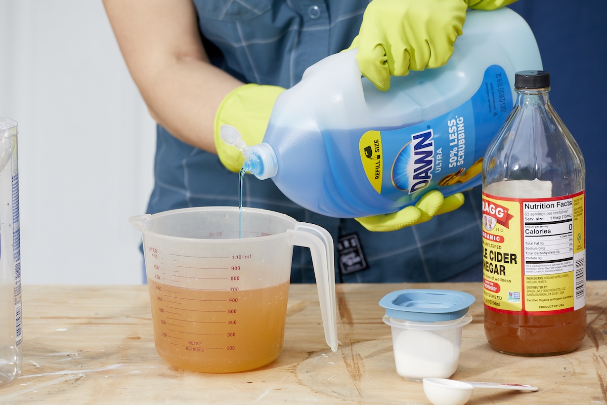 Woman pours dish soap into measuring cup full of apple cider vinegar.