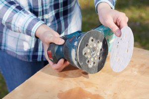 Woman attaches a sandpaper disc to a palm sander.