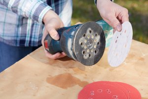 Woman holds a palm sander, testing out sandpaper discs with various grit levels.