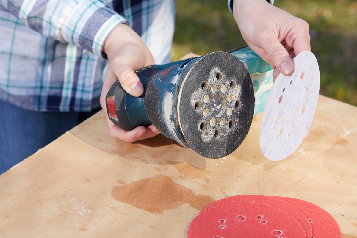 Woman holds a palm sander, testing out  sandpaper discs with various grit levels.