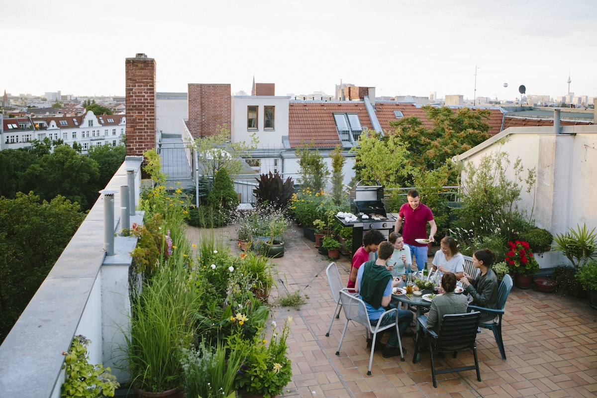 A group of people grilling food on a rooftop patio with a large garden.