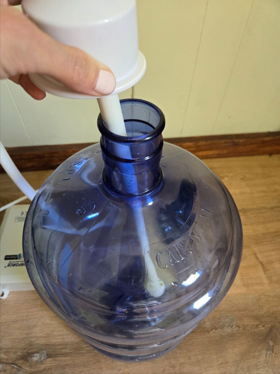 A person attaching an ice maker water line pump to a water storage tank.