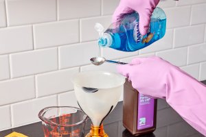 Woman adds dish soap to homemade grout cleaner recipe.