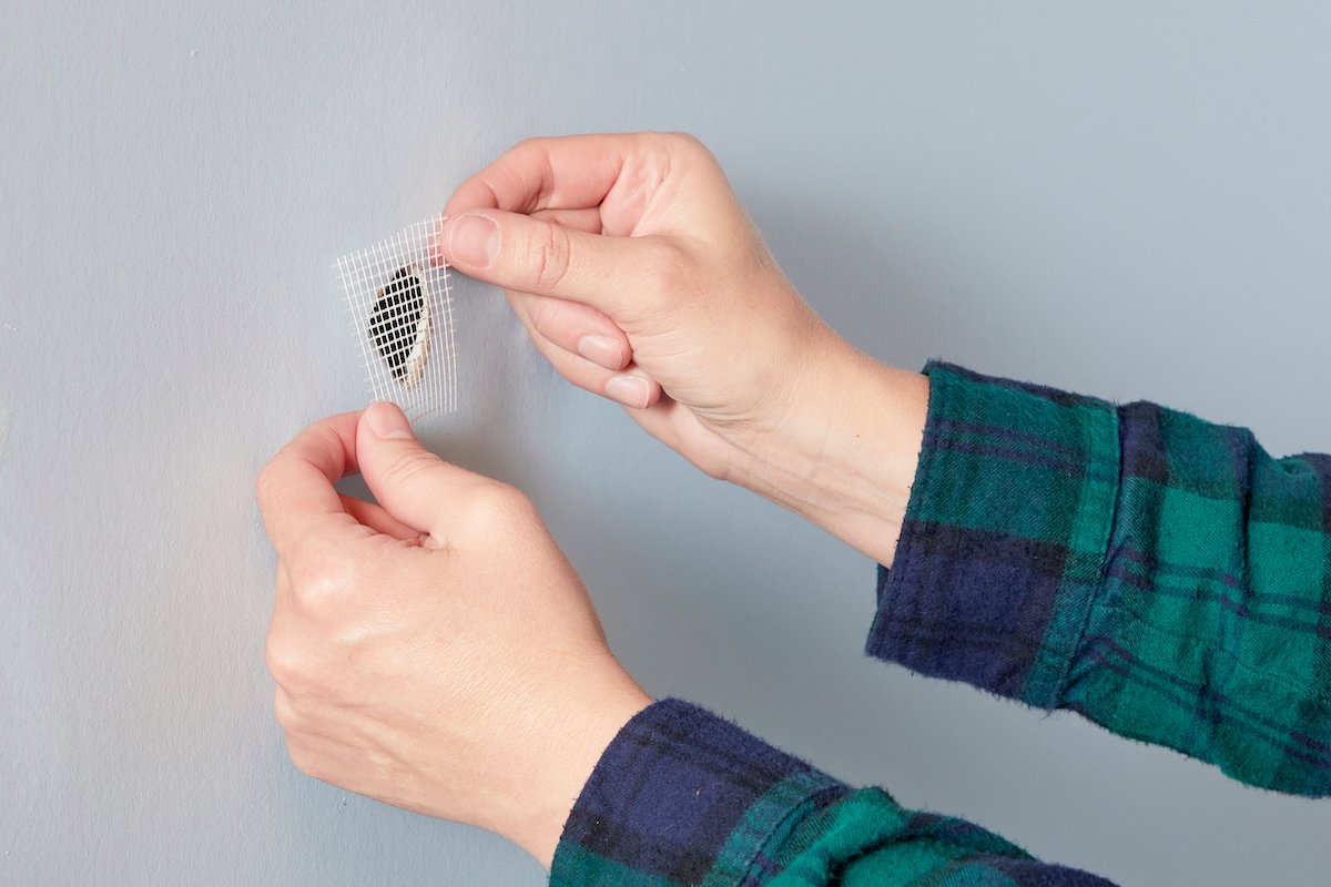 Woman covers a hole in drywall with drywall mesh tape.