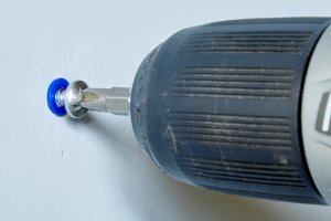 Using a drill to pull a screw a little bit out of a drywall anchor.